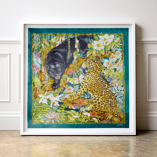 Framed Gucci Double Trouble silk scarf wall art featuring a black panther and spotted leopard amongst lush tropical flowers and botanical foliage. Luxury designer textile artwork hand-framed in a deep-set white shadow box frame and displayed against a white panelled wall.