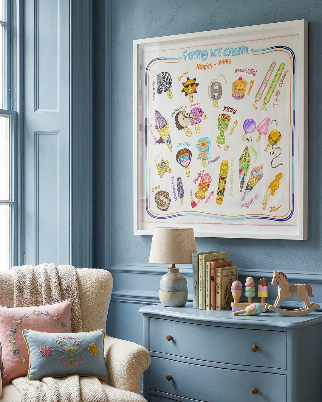 Colourful ice cream framed silk scarf artwork on a blue wall above a dresser in a child's room with toys and books.